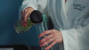 Tanımlanamayan iki kadının bardağa su döktüğü görüntüler. Beyaz bornozlu, sağlık içeceği içen bayan arkadaşlar. Sağlık programı, spa merkezinde diyet. Kapalı