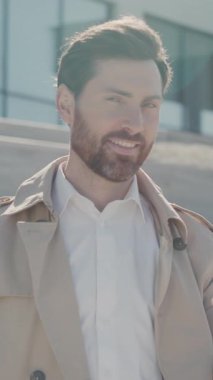 Palto giyen yakışıklı bir işadamı göl kenarındaki parkta akıllı telefon kullanıyor. Gülümseyerek etrafına bak. Kapatın. Yavaş çekim