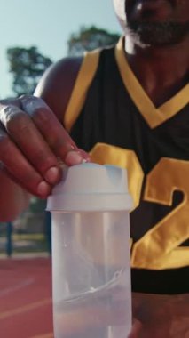 Çekici bir Afrikalı Amerikalı sokak basketbolcusunu eğittikten sonra açık hava çocuk parkında su içmek için mola verdi. Güneş ışığı var. Yaz. Spor. Mahkeme. Yavaş çekim