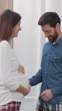 Genç sakallı adamın karısına karnını gösteriyormuş gibi yaptığı komik bir sahne. Hamile bir kadın. Eğlence ve mutluluk.