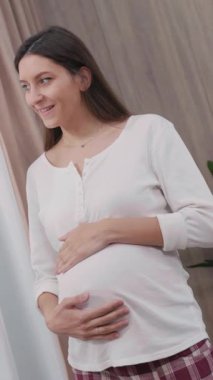 Beyaz, sağlıklı, güzel bir kadın hamile, bebek göbeği bekleyen, pencereden bakan. Daire. Sağlık Hizmetleri.