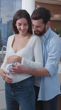 Kafkasyalı neşeli bir çift genç ebeveyn, sıcak mutfakta bebeklerine sarılıyorlar. Aile evde. Planlı hamilelik. Mutlu bir hayat. İlişki.