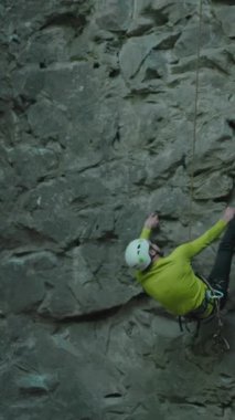 Genç sıska sporcu dağda clim eğitiyor, miğfer takıyor, ip kullanıyor ve kayalara tırmanıyor. Dağcı. Profesyonel dağcı. Ekstrem aktiviteler.