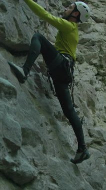 Aşırı yürüyüşçü, kasklı, sakallı, parlak sarı spor giyimli, kireçtaşı kayalıklara tırmanan genç adam..