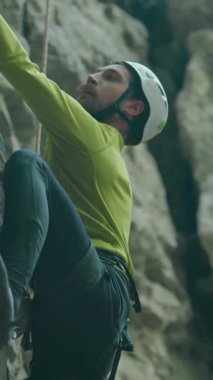 Kafkasyalı genç hippi dikkatlice kayaya tırmanıyor, sıkıca kavrıyor ve yukarı bakıyor. Sakallı sporcu. Aşırı hareketlilik. Yürüyüş.