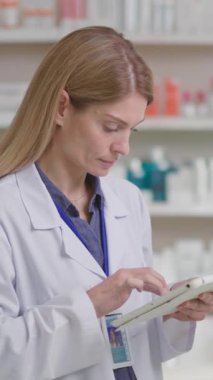 Kafkas sarışın olgun kadın eczanede ilaç reçetesi aramak için tablet bilgisayar aygıtı internet veritabanı kullanıyor..