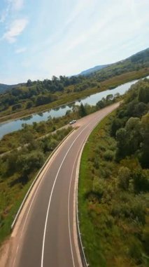 FPV, çarpıcı doğanın insansız hava aracı görüntüsü. Resimli kırsal vadide uzun otoyol kıvrımlı yollar. Yeşillik. Yaz sahnesi.