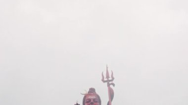 Tanınmış bir tanrının çarpıcı ve canlı kırmızı heykeli güzel bir atmosferik bulutlu zemine karşı dimdik ayakta duruyor.