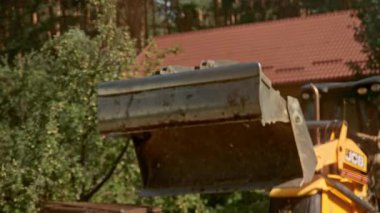 Bu videoda kırmızı çatılı büyüleyici bir evin önünde kiri hareket ettiren sarı bir buldozer, inşaat faaliyetleri ve JCB buldozer yer alıyor.