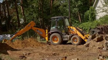 Bu inşaat sahnesinde bir kepçe, kazıcı ve traktör de dahil olmak üzere ağır makineler çalışıyor. Büyük bir çukur kazıyor ve modern verimliliği gösteriyor.