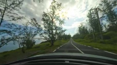 Ağaçların arasından süzülen güneş ışığıyla güzel bir yolda huzurlu bir yolculuğun tadını çıkar. Yol kenarına park edilmiş beyaz bir araba, sakin atmosfere katkı sağlar.