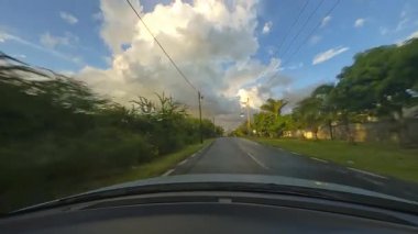 Bereketli ağaçlar ve canlı bir gökyüzü ile çevrili manzaralı bir yolda ilerleyen bir araba güzelliği yakalar.