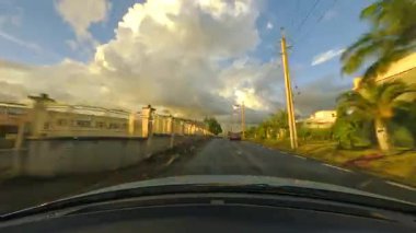 Bir araba yemyeşil ağaçlar arasında manzaralı bir yolda ilerliyor, bulutlu bir gökyüzünün altında huzurlu bir ortam yaratıyor, izleyicileri doğayı keşfetmeye çağırıyor güzellik