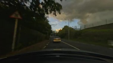 Bu büyüleyici video günbatımında ve bulutlu gökyüzünün altında özgürlük ve keşifleri çağrıştıran manzaralı manzaralarda seyahat eden bir arabayı gösteriyor.