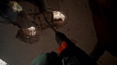 Toz ve molozlarla dolu bir duvarı delip geçen matkabın odaklanmış görüntüsü, yenileme çalışmaları sürüyor.