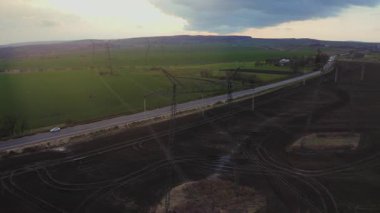 Tarım arazisi üzerinde uçan helikopter dronu yeşil kırsal alanda inşa edilmiş elektrik güç direklerinin yanından geçiyor. Hava manzarası.