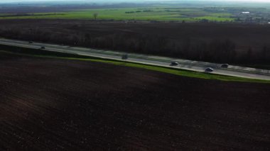 Helikopter tarım arazileri ve uzun otoban üzerinde uçuyor. Bir sürü araba geçip gidiyor. Kırsal manzaranın havadan görünüşü. Seyahat kavramı.