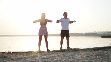 Çok ırklı yakışıklı bir sporcu ve plajda spor yapan bir kadın. Genç ve modern spor çifti birlikte trende eğleniyor. Doğa arkaplanı.