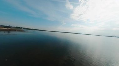 Su manzarası. FPV, yaz mevsiminde sonsuz güzel göl manzarasının insansız hava aracı görüntüsü. Genç turistler su üstünde sörf yapıyor. Seyahat kavramı.