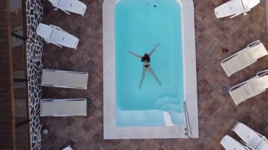 Hava aracı otelin açık mavi havuz suyunda yüzen genç bir kadını vurdu. Tropikal adadaki pahalı villanın yukarıdan görünüşü.