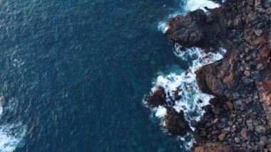 Beyaz köpüklü dalgaları, kayalık kıyıları ve kayalık uçurumları olan derin mavi deniz manzarasının sinematik drone görüntüsü. Dağlık tropikal ada manzarası.