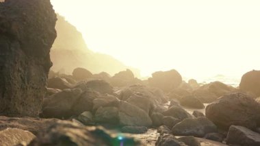 Karanlık kayalıklarla dolu harika, boş bir kumsalın muhteşem seyahat çekimi. Güzel sahil manzarası ve gün batımı. Yeni yerler keşfetmek. Tatil kavramı.