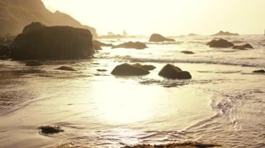 Vahşi okyanus sahilleri, karanlık kıyı kayaları ve muhteşem kayalıklar. Deniz kenarında gün batımına ilham veren portakal. Okyanus tatili. Sinematik görünüm.