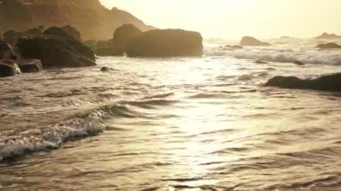 Deniz kenarında sinematik sarı günbatımının güzel bir videosu. Sakin deniz, huzurlu beyaz dalgalar ve siyah kayalar. Sahil yolculuğu. Yaz tatili. Seyahat kavramı.