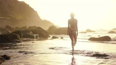 Sahilde yürürken seksi bikini mayo giyen alımlı genç bir kadının silueti. Güzel güneşli hava, gün batımı ve sakin doğa..