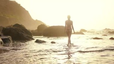 Genç bir kadın sahil boyunca güzel bir gün batımında yürüyor. Kırmızı bikini mayo giyen seksi kız deniz kenarında manzarayı izliyor. Resimli denizde gün batımı.