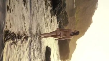 Gün batımında sahildeki kayalıklarda yürüyen seksi bikinili mutlu genç kız. İnsanlar, tatiller ve duygular. Güzel doğa..