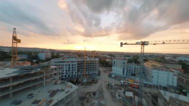 FPV insansız hava aracı günbatımında harika bir çağdaş şehrin üzerinde uçuyor. Gelecekteki modern konut binalarının inşaat alanının görüntüsü.