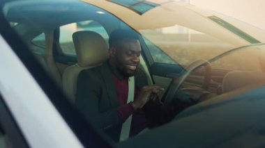 Los Angeles, California 1503 EDITORIAL: Gülümseyen Afro-Amerikan genç işadamı direksiyonda telefonu kullanıyor genç gülümseme aracının arkasında oturuyor yolcu koltuğu açık otomobil sokağı otomobil işadamı ceketini yavaş çekimde satın alıyor