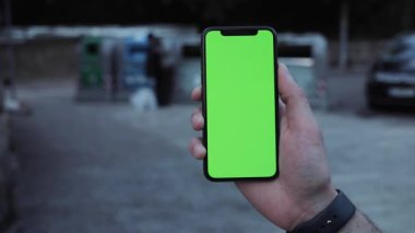 NEW YORK - 5 Nisan 2018: Elinde yeşil ekran telefon tutan bir adama yakın plan Akşamları sokakta modern bir cihaz kullanarak akıllı telefon taklidi yapmak.