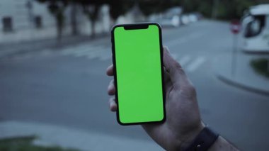 NEW YORK - 19 Nisan 2019: Dikey yeşil ekran mobil arka plan araba yolu akşam görüşü olan telefonu kullanarak erkek ellerini kapat bulanık krom anahtar değiş tokuş yaparak açık ekran dokunmatik dokunmatik internet dokunuşunu yavaş çekimde göster