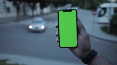 NEW YORK - 19 Nisan 2019: Yavaş çekim adamı elleri dikey yeşil ekran mobil arka plan araba yol görüşlü telefon kullanıyor akşam görüşü bulanık kromaanahtar değiş tokuş yapıyor açık hava dokunmatik ekranı internet dokunuşu