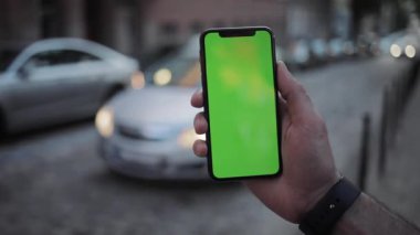 NEW YORK - 19 Nisan 2019: Akşamları, dikey yeşil ekranlı, mobil arka planlı, otomobil yol manzaralı telefon kullanan şehir görüntüsü bulanık kromaanahtar değiş tokuş eden dokunmatik ekran açık hava iş dünyası yavaş çekim interneti