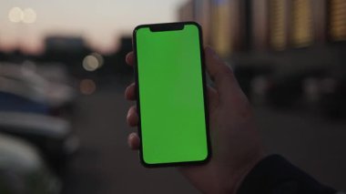 NEW YORK - 19 Nisan 2019: Adam elini kapatıyoruz. Gece şehir ışık arka planında dikey yeşil ekranlı akıllı telefon kullanıyoruz. Dijital araç iletişim cihazı.