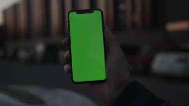 NEW YORK - 19 Nisan 2019: Adam el ele tutuşuyor, şehrin arka planında dikey yeşil ekranlı akıllı telefon kullanıyor, dijital cihaz, dokunmatik telefon, yavaş çekimde trafiği kapatıyor.