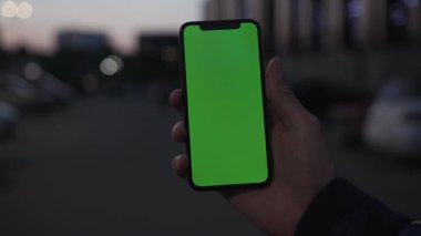 NEW YORK - 19 Nisan 2019: Elle tutulan eller, şehrin arka planında dikey yeşil ekranlı akıllı telefonu, gece lambası iletişim cihazı dijital cihaz, dokunmatik telefon, yakın çekim mobili