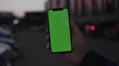 NEW YORK - 19 Nisan 2019: Adam, şehrin arka planında dikey yeşil ekranlı akıllı telefon kullanıyor. Dijital cihaz, ekrandaki mobil trafiği kapatıyor.