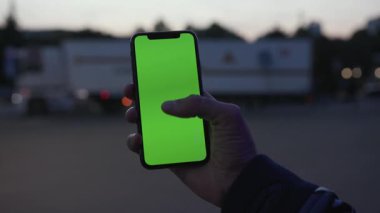 NEW YORK - 19 Nisan 2019: Elinde akıllı telefonu olan ve gece lambası arka planında dikey yeşil ekranlı akıllı telefonu kullanan bir adam dijital cihaz, mobil dokunmatik ve yavaş çekimde trafiğe duyarlı cep telefonu veriyor