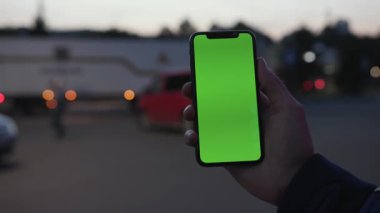 NEW YORK - 19 Nisan 2019: Elinde akıllı telefon bulunan ve gece şehir ışıklarındaki yeşil ekran araba iletişimi cihazını kullanan adam dijital cihaz, cep telefonuna dokunmatik mobili kapatıyor