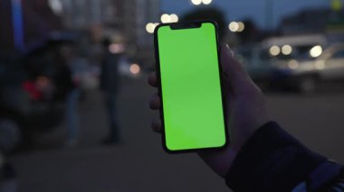 NEW YORK - 19 Nisan 2019: Arka plandaki arabacı, gece şehir ışığı iletişim cihazında dikey yeşil ekranlı akıllı telefon kullanarak dijital cihaz, cep telefonu, yakın çekim ekranı,