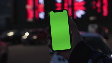 NEW YORK - 19 Nisan 2019: Elinde akıllı telefonu olan ve gece şehir renklerinde yeşil ekranlı akıllı telefonu kullanan bir adam dijital cihaz, mobil dokunmatik, mobil, yavaş çekimde araç iletişimi cihazını teslim etti
