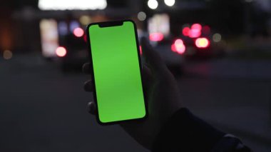 NEW YORK - 19 Nisan 2019: Elinde akıllı telefon bulunan ve gece lambası arka planında dikey yeşil ekranlı araba iletişimi cihazını kullanan adam dijital cihaz, mobil dokunmatik mobil mobil ağır çekim