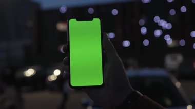 NEW YORK - 19 Nisan 2019: Elle tutulan eller gece şehir renkli açık renk arka plan iletişim cihazına dikey yeşil ekranlı akıllı telefonu kullanarak dijital cihaz telefon dokunmatik mobil mobil ağır çekim