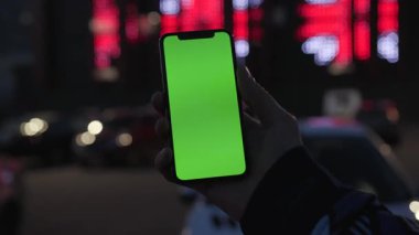 NEW YORK - 19 Nisan 2019: Renkli ışıklı adam elinde dikey yeşil ekranlı akıllı telefon kullanıyor ve gece şehir ışık arka planında araç iletişimi cihazı dijital cihaz telefon dokunmatik mobil ağır çekim