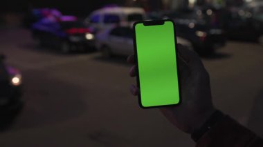 NEW YORK - 19 Nisan 2019: Elle tutulan eller gece şehir renkli açık renk arka plan iletişim cihazına dikey yeşil ekranlı akıllı telefonu kullanarak dijital cihaz telefon dokunmatik mobil mobil ağır çekim