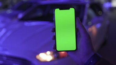 NEW YORK - 19 Nisan 2019: Genç adam elinde dikey yeşil ekranlı akıllı telefonu gece mavi ışıklı arka plan beyaz araba iletişimi aygıtı ile dijital ekranlı mobil dokunmatik telefon yavaş çekim